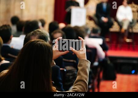 Una donna scatta una foto con un telefono cellulare in una riunione Foto Stock