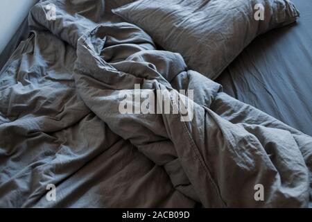 Grigio di un foglio di cotone e coperte con cuscini sul letto Foto Stock