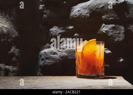 Un cocktail di colore arancione nella barra di colore scuro. Un alcol bevande con ghiaccio su un tavolo di legno. Bevanda fresca in un elegante vetro. Pezzo di arancione e il ghiaccio. Foto Stock