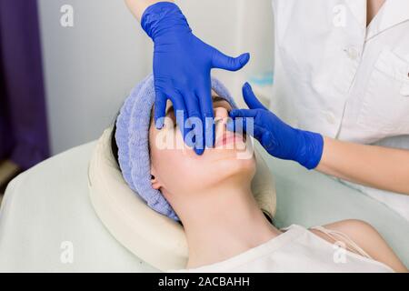 Giovane bella ragazza con massaggio viso rilassante nella spa salone. Immagine di donna in spa salone giacente sulla scrivania di massaggio Foto Stock