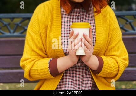 Una donna è seduta su una panchina nel parco e tenendo una tazza di bambù Foto Stock