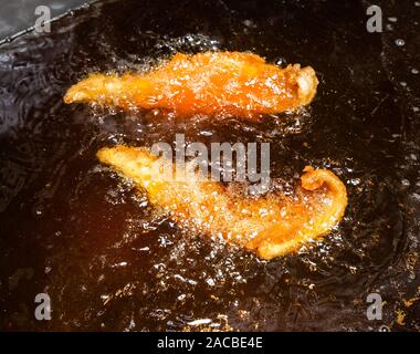 Cucina del pesce in una friggitrice ad alto contenuto di grassi in un negozio di pesce e patatine nel Regno Unito Foto Stock