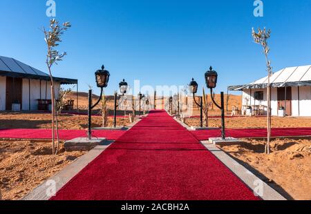 Tappeto rosso percorso principale tra le tende di lusso Golden Campeggio nel deserto del Sahara, Merzouga Marocco in una giornata di sole Foto Stock