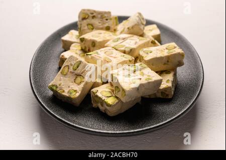 Orientale torrone arabo dolcezza con pistacchi su un nero piastra in ceramica su uno sfondo luminoso. Vista frontale Foto Stock