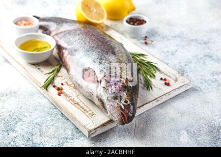 Fresco iridato materie Trote alle erbe rosmarino, pepe, olio d'oliva, sale himalayano e limone su sfondo chiaro. Cibo sano. Concetto di cucina a vista. Foto Stock