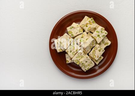 Orientale torrone arabo dolcezza con pistacchi su un marrone piastra ceramica su uno sfondo luminoso. Vista superiore Foto Stock