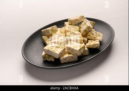 Orientale torrone arabo dolcezza con pistacchi su un nero piastra in ceramica su uno sfondo luminoso Foto Stock