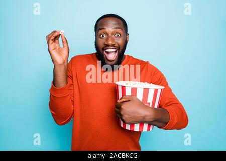 Foto di divertenti atonished mixed-gara crazy estasiato urlando uomo guarda la serie televisiva e sorpreso la trama tenendo popcorn sorridente della benna Foto Stock