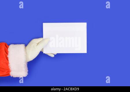 Mano di santa claus tenendo un cartello bianco su sfondo blu. Shopping, vendite, dando dono del Natale e del nuovo anno concetti. Foto Stock