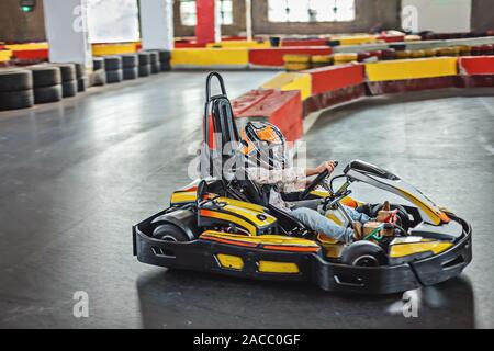 Intrattenimento per bambini in ambienti chiusi. Ragazza la guida go kart su pista. Uno stile di vita attivo. Foto Stock