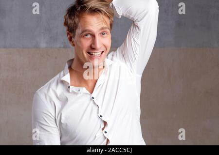 Ritratto di un giovane positivo e fiducioso in una classica camicia bianca. Felice studente ragazzo, ritratto contro muro grigio testurizzato. Foto Stock