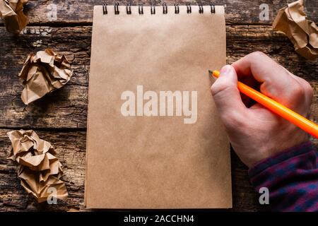 Uomo scrive in un notebook su un sfondo di legno Foto Stock