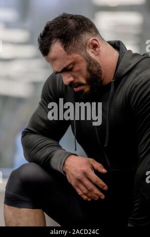 Uomo Barbuto appoggiata sul ginocchio durante la pausa di riposo durante il crossfit allenamento in palestra Foto Stock