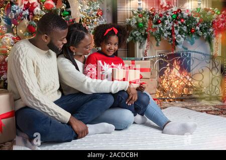 Carino piccolo nero ragazza ricevute regalo di Natale da i suoi genitori Foto Stock