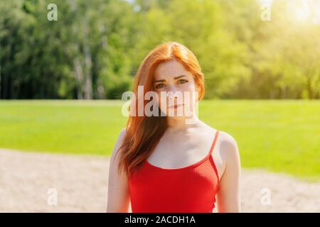 Giovane donna indossa red strappy top all'aperto in un parco su un luminoso giorno di estate Foto Stock