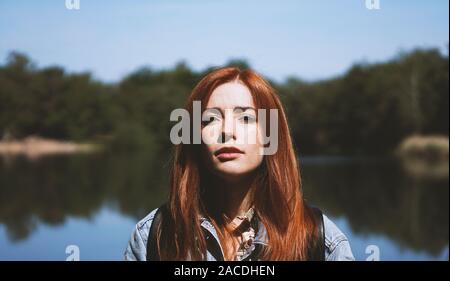 Campestre giovane donna in piedi dal lago nella luce cruda con ombre profonde - autentico gente reale nozione