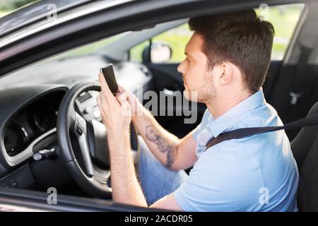 Uomo alla guida di auto e utilizza lo smartphone Foto Stock