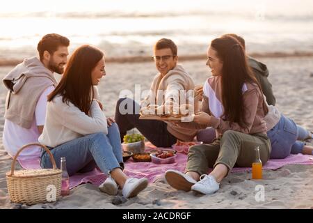 Happy amici mangiando panini al picnic sulla spiaggia Foto Stock