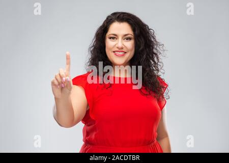 Donna felice in abito rosso che mostra un dito Foto Stock