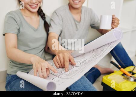 Close-up di immagine sorridente coppia giovane a bere caffè e discutere il piano di costruzione della loro nuova casa Foto Stock