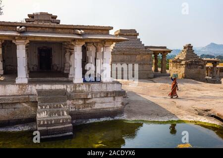 Bella vista delle rovine con un piccolo laghetto. Ragazza indiana passeggiate fra gli edifici antichi. Monumento nel gruppo di Hampi, Karnataka, India Foto Stock