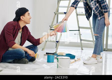 Sorridente giovane uomo asiatico punta al colore nella tavolozza di campioni in mano della ragazza e la scelta di ombra per pareti camera da letto Foto Stock