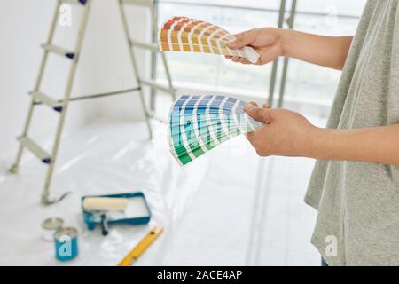 Carta palletes di campioni di vernice nelle mani della persona scelta di colori per pareti in un nuovo appartamento Foto Stock