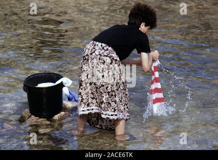 9 agosto 1993 durante l'assedio di Sarajevo: una donna lava biancheria nel fiume Miljacka, appena più a monte dalla Galleria Nazionale di Arte Moderna e la libreria. Foto Stock