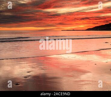 Charmouth, Dorset, Regno Unito. 2° dicembre 2019. Regno Unito Meteo: colori spettacolari sono riflesse nella sabbia bagnata a bassa marea al tramonto lungo la spiaggia del resort costiero di Charmouth. Orme nella sabbia bagnata sono state il solo segno di vita su una spiaggia deserta. Credito: Celia McMahon/Alamy Live News. Foto Stock