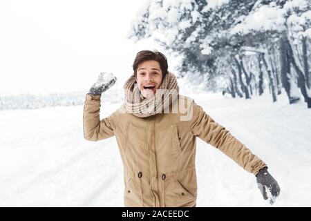 Felice giovane uomo gettando Snowball guardando la fotocamera nella foresta Foto Stock