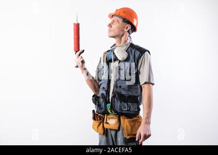 Un builder in un casco con silicone in una pistola di montaggio. Tiene in mano. Su uno sfondo luminoso. Foto Stock