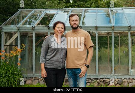 Sorridente giovane con la zia di fronte una serra di vetro vicino casa estiva Foto Stock