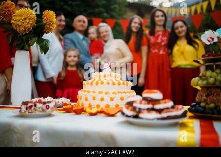 Festa di famiglia compleanno baby al di fuori nel cortile.Grande party in giardino. Il fuoco selettivo sulla torta con una candela 5 anni, offuscata la gente grande Foto Stock