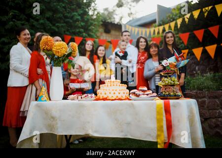 Festa di famiglia compleanno baby al di fuori nel cortile.Grande party in giardino. Il fuoco selettivo sulla torta con una candela 5 anni, offuscata la gente grande Foto Stock