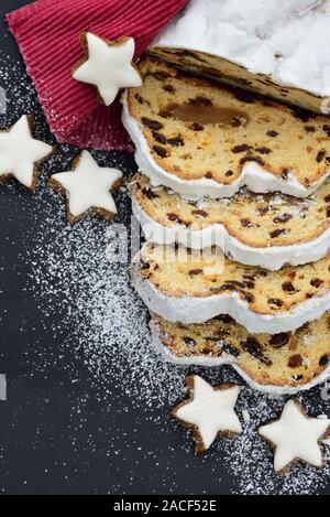 Un Natale tedesco tradizionale torta, un stollen con biscotti a forma di stella e zucchero in polvere contro uno sfondo scuro Foto Stock