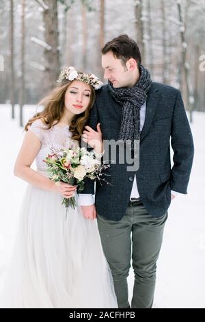 Coppie in viaggio di nozze di close-up. Sposa con il bouquet, con cotone corona, e groom sullo sfondo di un paesaggio invernale, foresta con la neve. Foto Stock