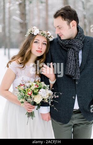 Coppie in viaggio di nozze di close-up. Sposa con il bouquet, con cotone corona, e groom sullo sfondo di un paesaggio invernale, foresta con la neve. Foto Stock