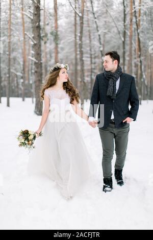 Sposa e lo sposo sono alla ricerca di ogni altro e passeggiate nella foresta d'inverno. Close-up. In inverno la cerimonia di nozze Foto Stock