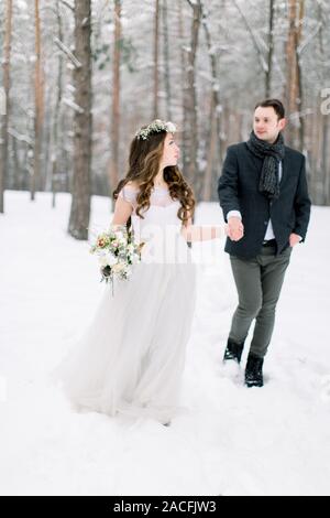 Sposa e lo sposo sono alla ricerca di ogni altro e passeggiate nella foresta d'inverno. Close-up. In inverno la cerimonia di nozze Foto Stock