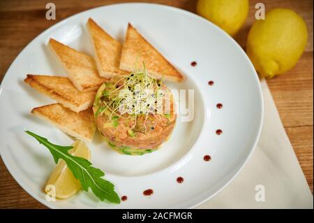 Deliziosa tartare di salmone con avocado. Disposizione con un bicchiere di vino e posate Foto Stock