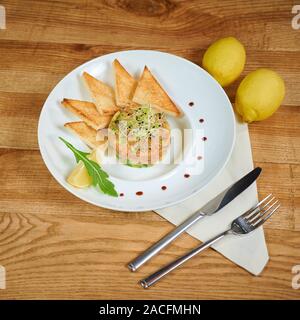 Deliziosa tartare di salmone con avocado. Disposizione con un bicchiere di vino e posate Foto Stock