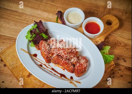 Serve delle deliziose ALI DI POLLO PICCANTI con semi di sesamo e salsa al peperoncino dolce bianco sul pannello di legno Foto Stock