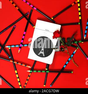 Piatto layout laici notebook bianco Parigi e red rose su sfondo rosso con colorate matite per ufficio. Il giorno di San Valentino card concetto di celebrazione romantica. Marzo 08 Womens giorno. Piatto, laici close up. Foto Stock