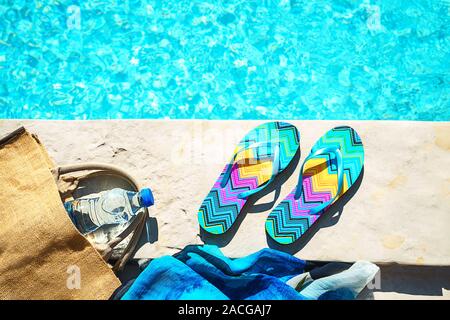 La piscina e il cappello di paglia, colorato flip flop, borsa di vimini, cappello di paglia, bottiglia con acqua ancora come sunny estate sfondo. Vacanze viaggi abbronzatura di Concetto di vacanza. Appartamento laico, vista dall'alto, vicino. Foto Stock