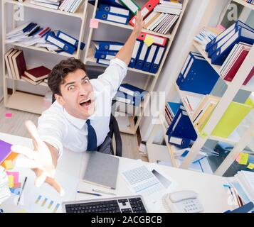 Imprenditore lavora in ufficio con pile di libri e giornali facendo di documenti cartacei Foto Stock