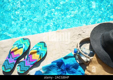 La piscina e il cappello di paglia, colorato flip flop, borsa di vimini, cappello di paglia, bottiglia con acqua ancora come sunny estate sfondo. Vacanze viaggi abbronzatura di Concetto di vacanza. Appartamento laico, vista dall'alto, vicino. Foto Stock