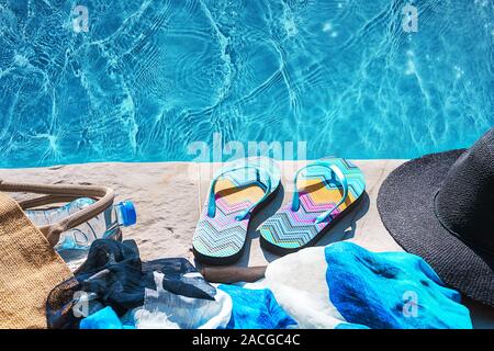 La piscina e il cappello di paglia, colorato flip flop, borsa di vimini, cappello di paglia, bottiglia con acqua ancora come sunny estate sfondo. Vacanze viaggi abbronzatura di Concetto di vacanza. Appartamento laico, vista dall'alto, vicino. Foto Stock
