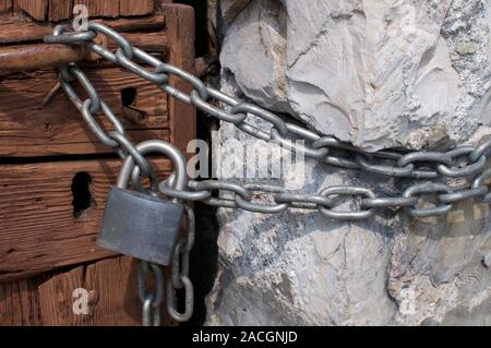 Chiudere l immagine di un lucchetto vicino con una robusta catena di metallo su una bella porta di legno su una vecchia casa in un villaggio nel nord Italia Foto Stock
