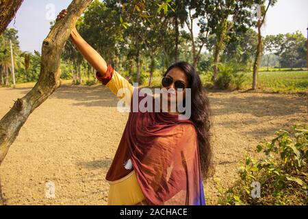 Ritratto di un carino,marrone,giocoso ragazza (bangladese o sud asiatico), nei pressi di un albero che ha lunghi capelli belli, lasciare vuoto il campo e gli alberi in background Foto Stock