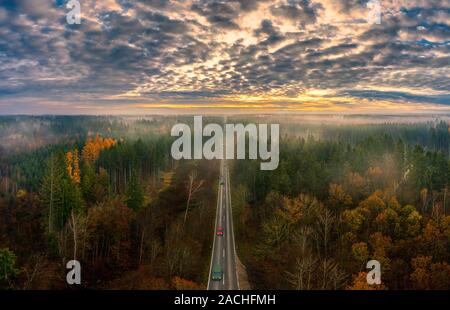 La splendida vista su una strada incorniciata da alberi autunnali con vista sulle montagne sullo sfondo. Foto Stock